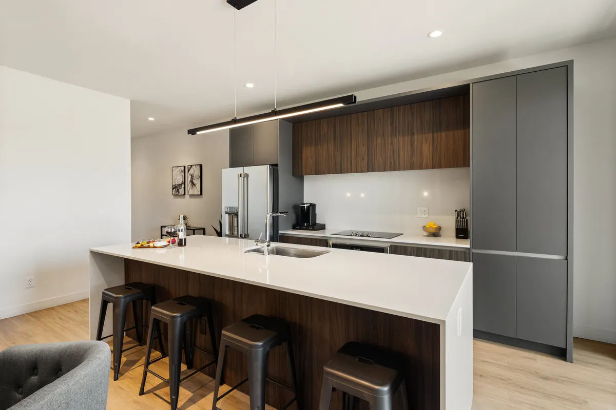 A stylish, modern kitchen featuring an island countertop with stools, kitchen appliances, and attractive wall art. The space is bright, functional, and welcoming, suggesting thoughtful design and readiness for cooking or entertaining.