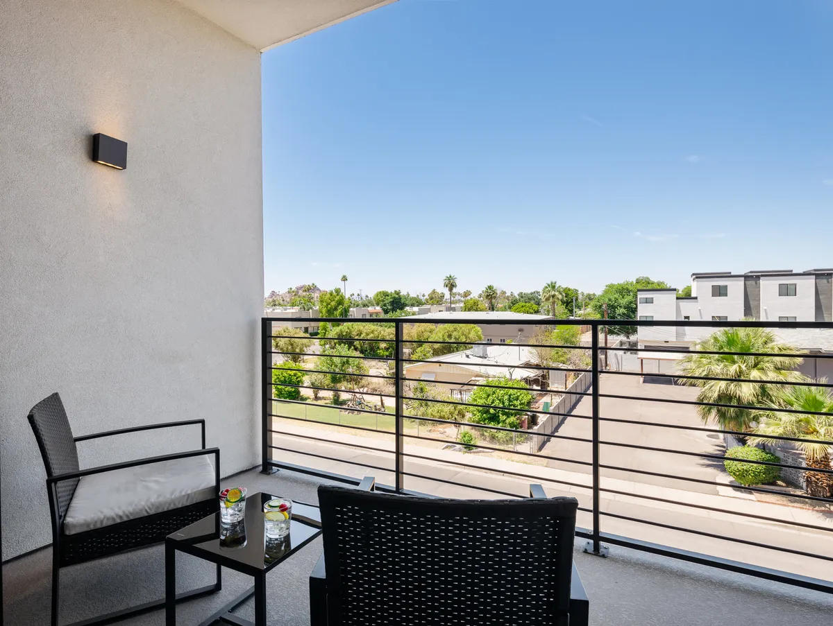 This image features a balcony seating area with comfortable chairs, decorative plants, and a view of the city skyline. The ambient lighting and inviting setup suggest a quiet space perfect for relaxing with a drink or enjoying intimate moments while taking in the surrounding urban scenery.