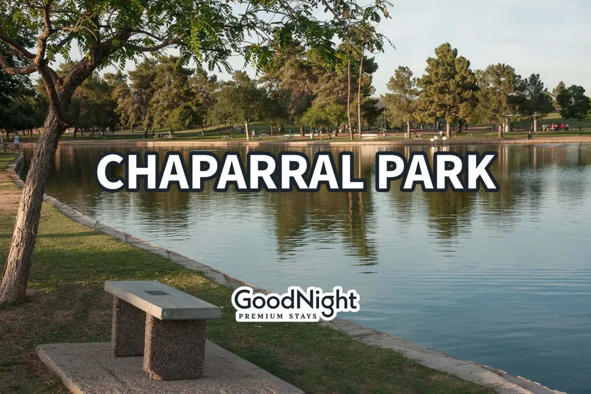 A peaceful lakeside park scene with a lake bordered by trees and a park bench in the foreground, inviting visitors to enjoy picnicking, walking, or simply relaxing in nature. The calm water and greenery suggest an ideal nearby recreation spot for families and pet owners.
