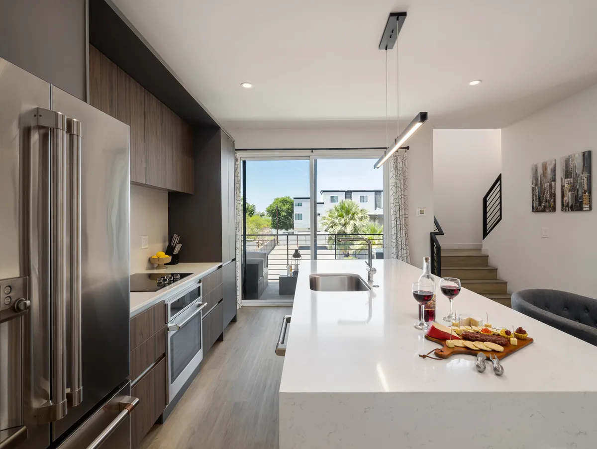 An open kitchen with a spacious island counter, set with wine glasses and a charcuterie board, complemented by high-end appliances and a sliding glass door. The scene exudes a welcoming, contemporary vibe, ideal for both cooking and entertaining.
