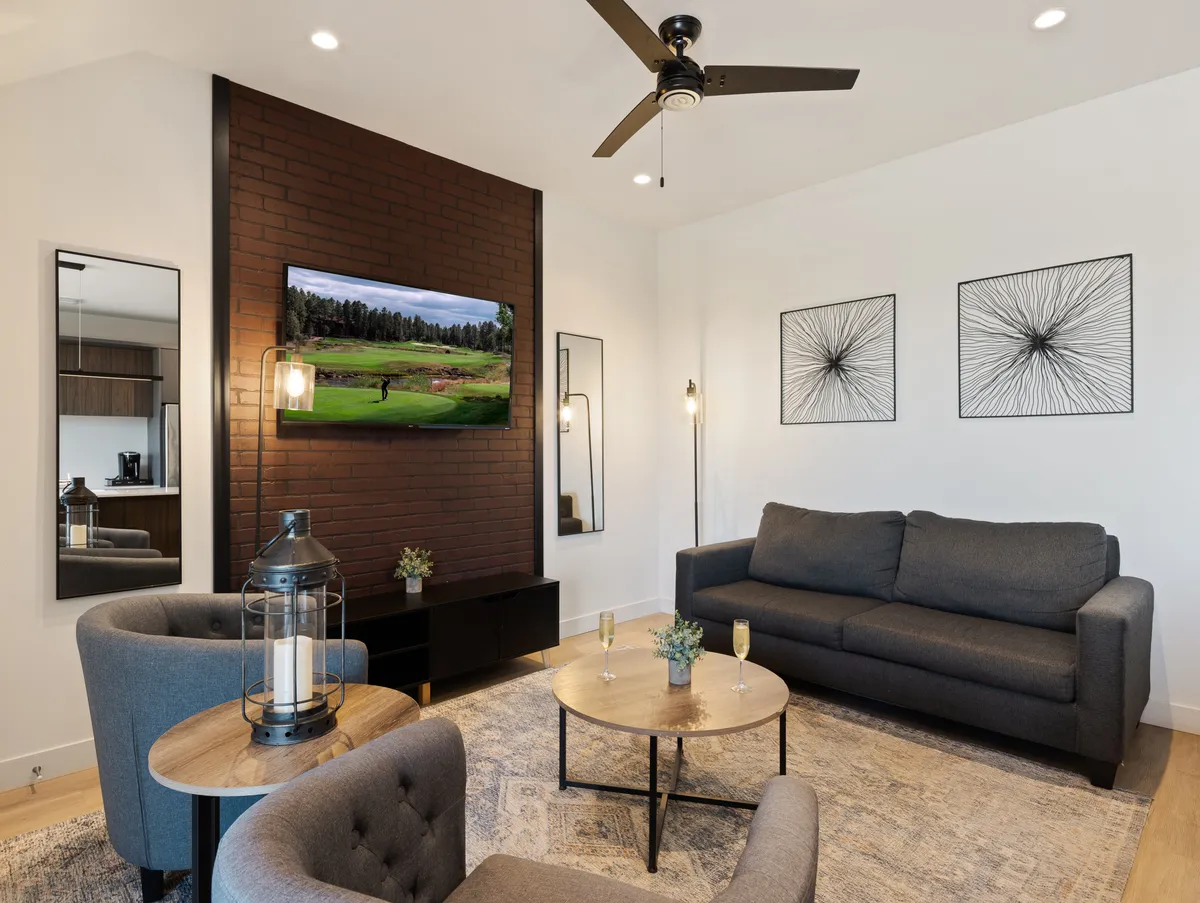 A contemporary living room with a comfortable gray sofa, brick accent wall featuring a mounted TV, stylish coffee table, and tasteful wall art. The inviting space is set for relaxation, socializing, or entertainment, embodying the modern and welcoming tone described in the section.