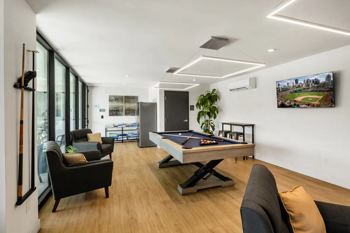 A stylish clubhouse interior featuring a pool table, modern sofas, a wall-mounted TV, and inviting lighting. The setup is perfect for evening socializing, with areas for games, watching sports, or relaxing with friends after a night out.