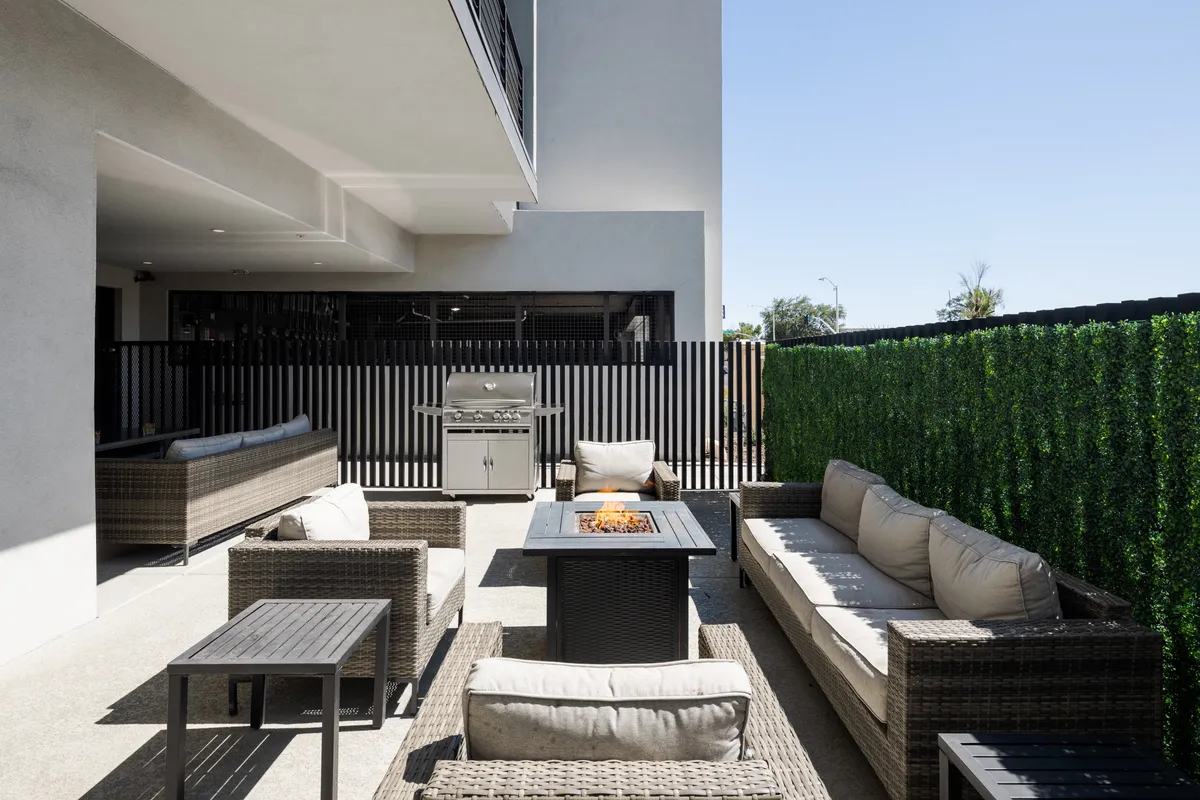 An inviting outdoor space featuring a fire pit surrounded by comfortable seating, a grill for barbecuing, lush greenery, and secure fencing. The setting is perfect for socializing and relaxing outdoors with friends or neighbors.